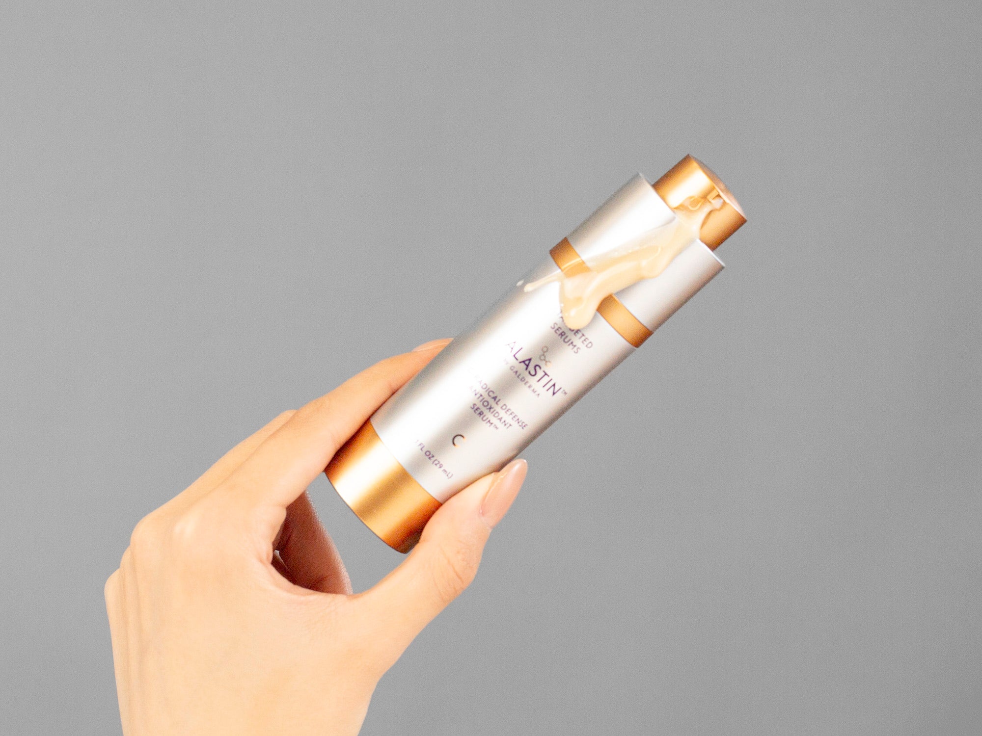 Laziza from LAZ Skincare's hand holding a bottle of lastin C-Radical Defense Antioxidant Serum against a neutral background