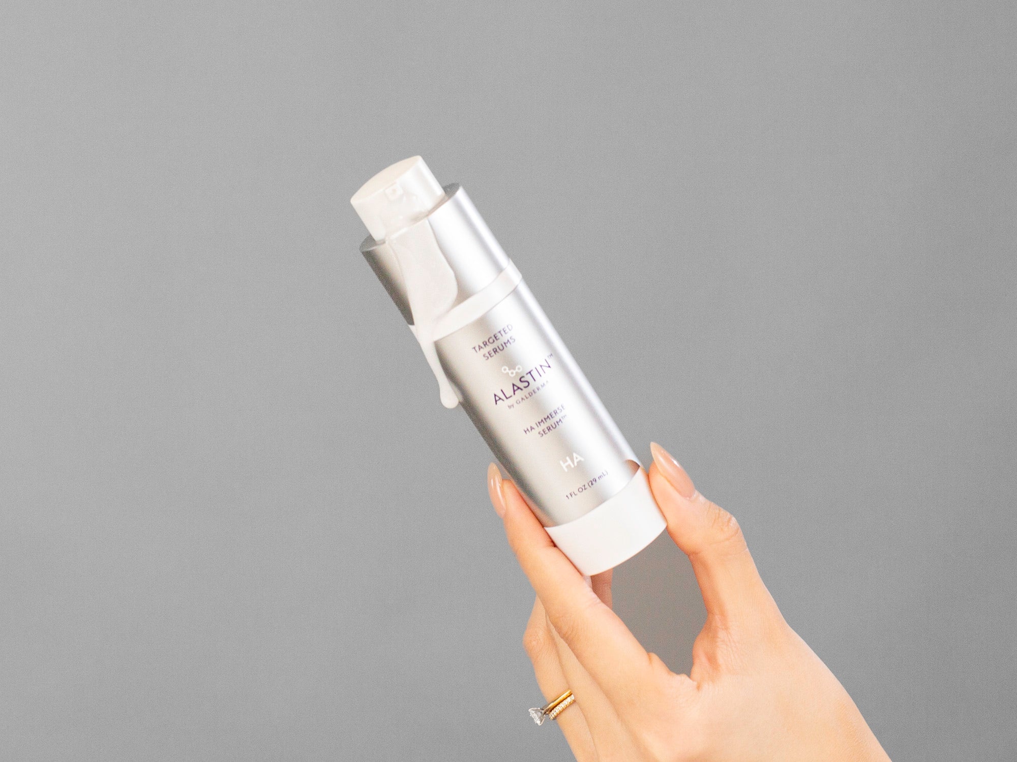 Laziza from LAZ Skincare's hand holding a silver bottle of Alastin HA Immerse Serum against a neutral background