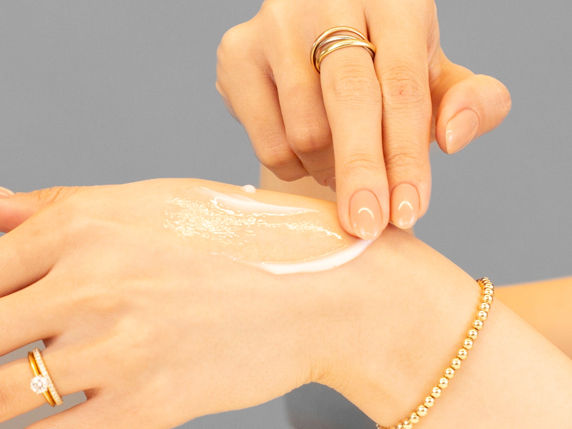 Hand applying Alastin Resorative Skin Complex to another hand with a gray background