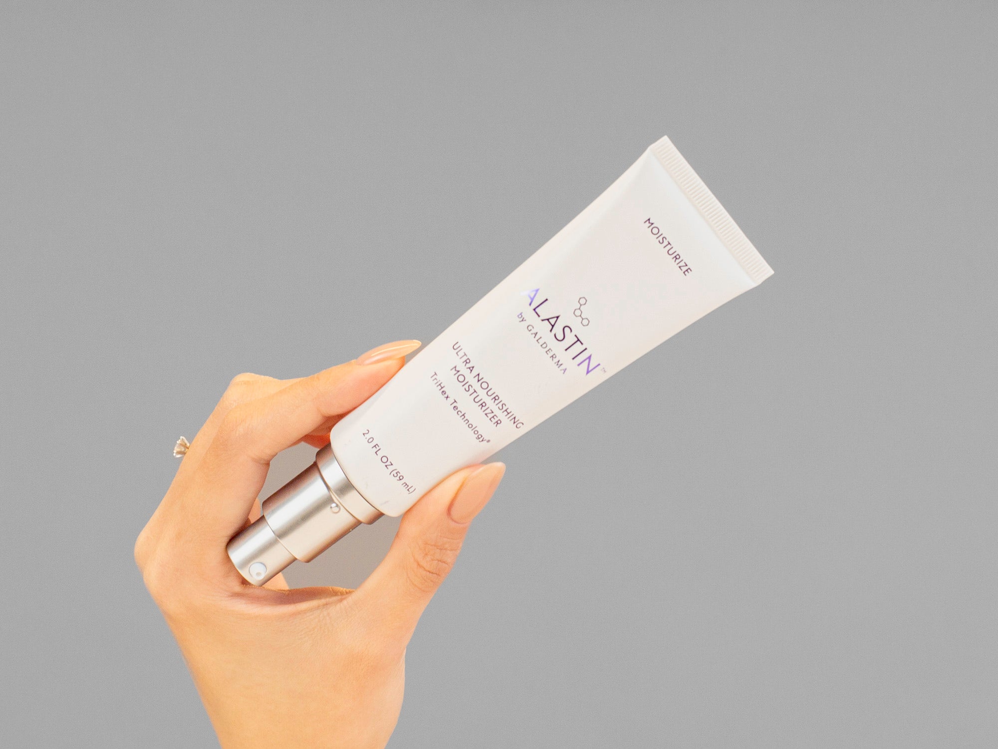 Laziza from LAZ Skincare holding a bottle of Alastin Ultra Nourishing Moisturizer against a gray background