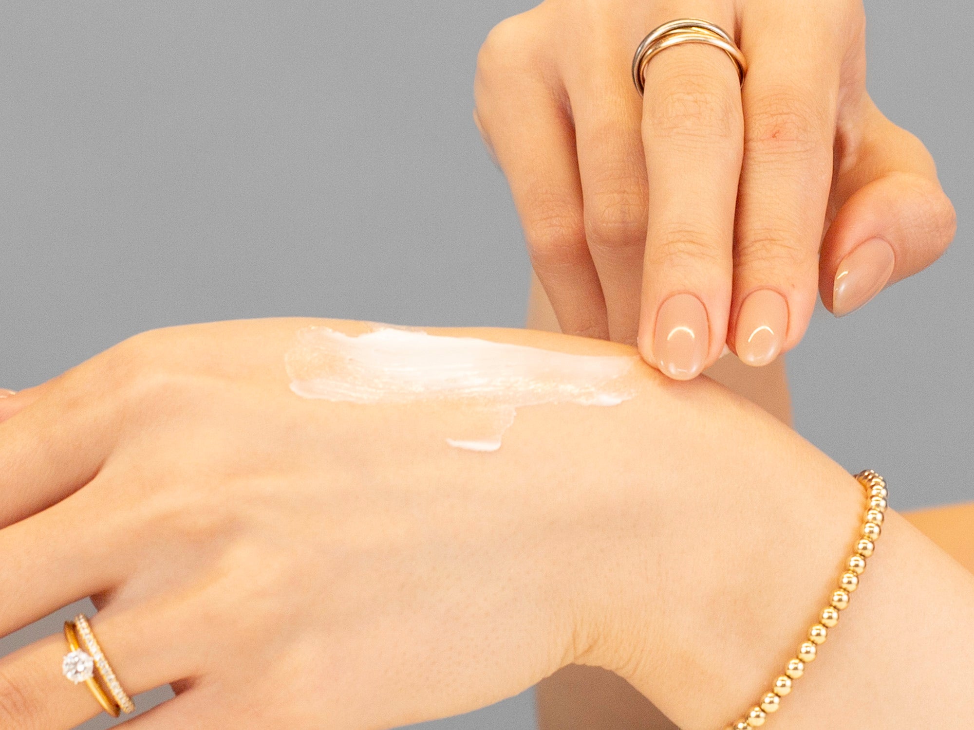 Laziza from LAZ Skincare applying Alastin Ultra Nourishing Moisturizer cream to another hand with a gray background