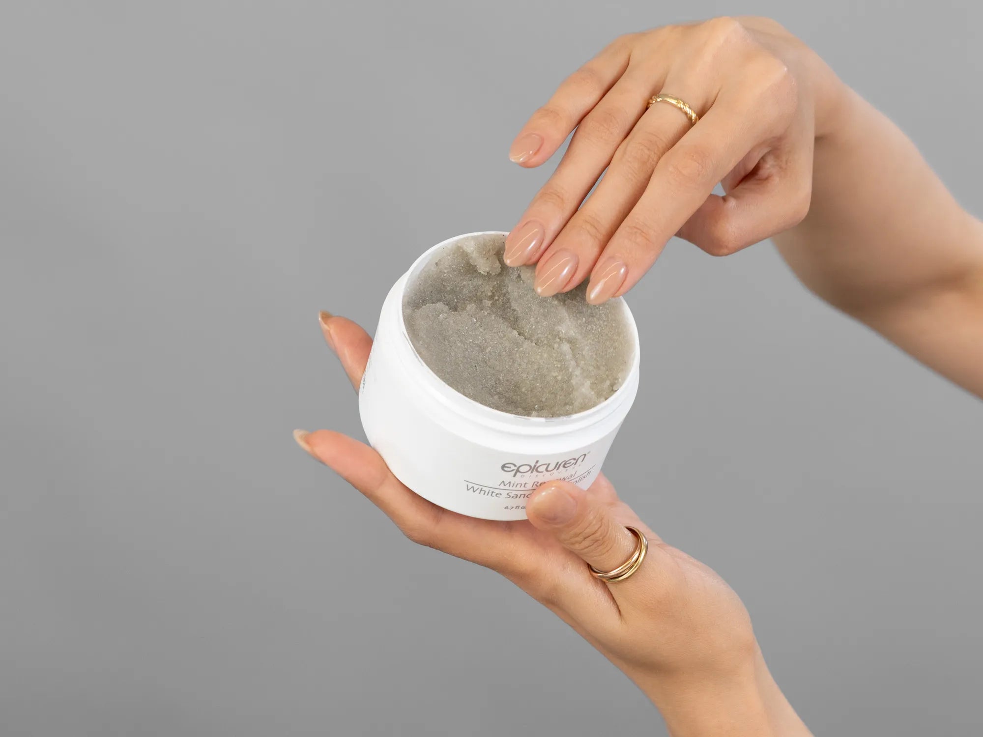Closeup of Laziza from LAZ Skincare holding up a bottle of Epicuren Mint Renewal White Sand Body Polish