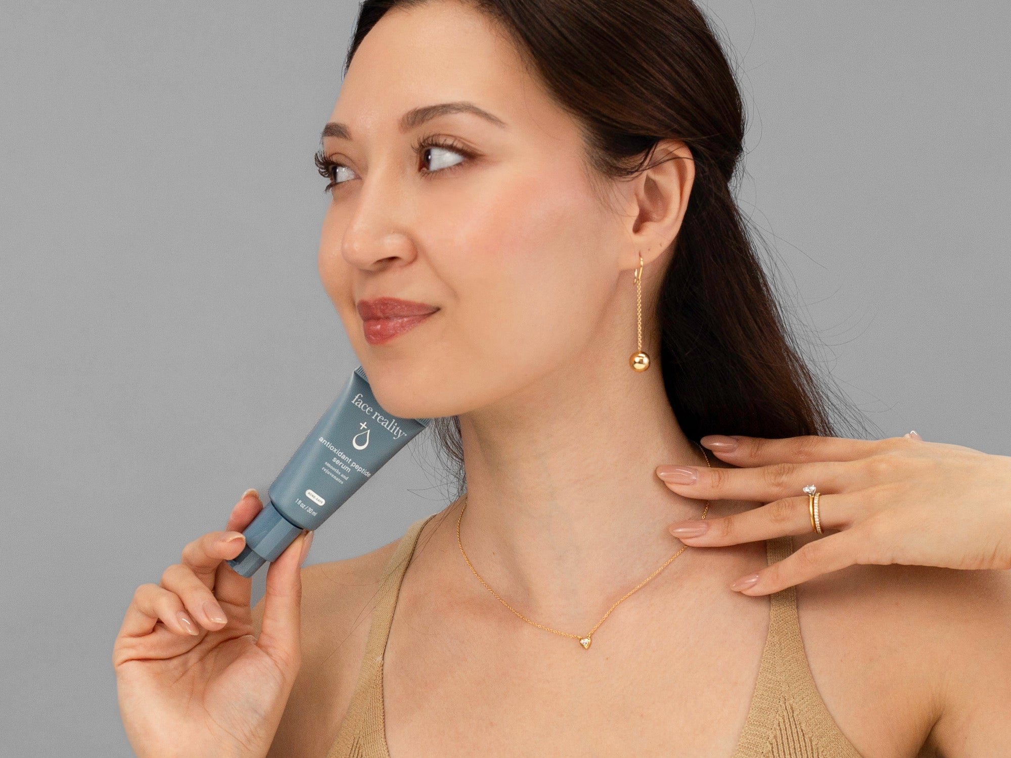 Laziza from LAZ Skincare holding a tube of Face Reality Antioxidant Peptide Serum up to her face