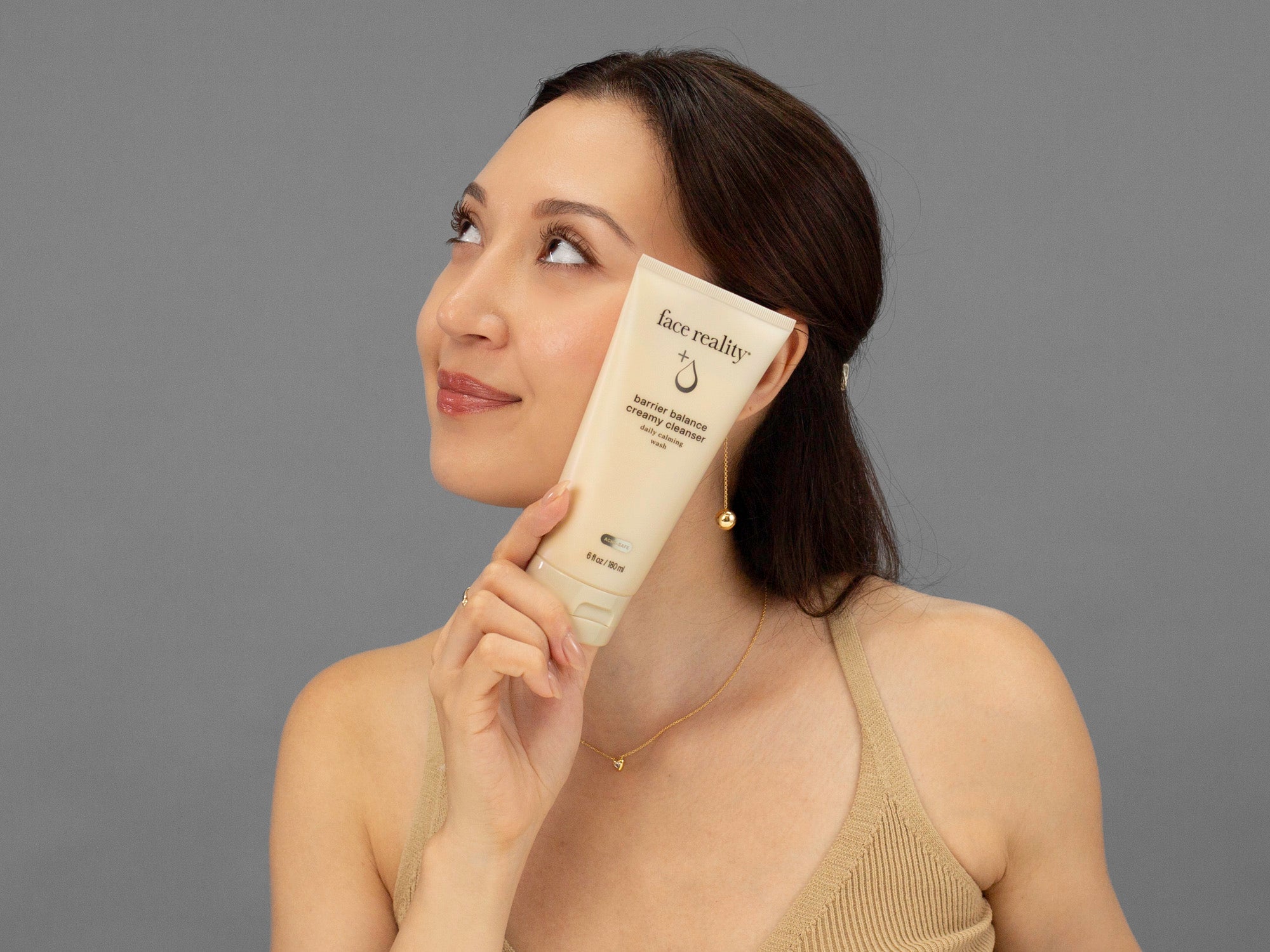 Laziza from LAZ Skincare holding a tube of Face Reality Barrier Balance Creamy Cleanser up to her face