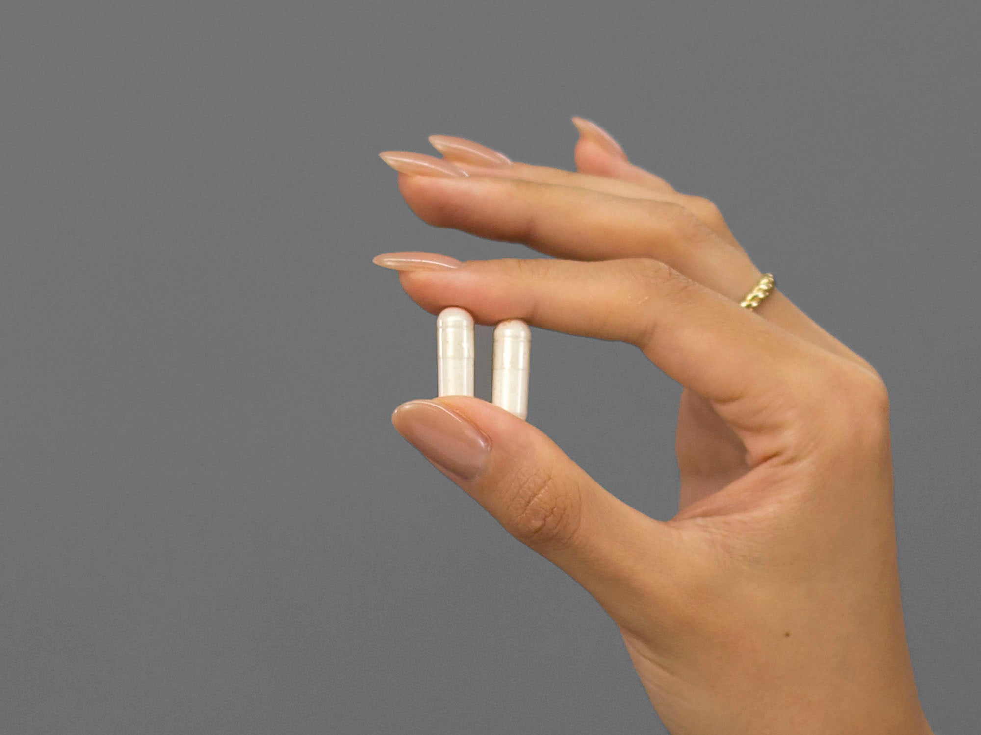 Closeup of Laziza from LAZ Skincare holding two capsules of Face Reality Clear Skin Restore supplements in her hand