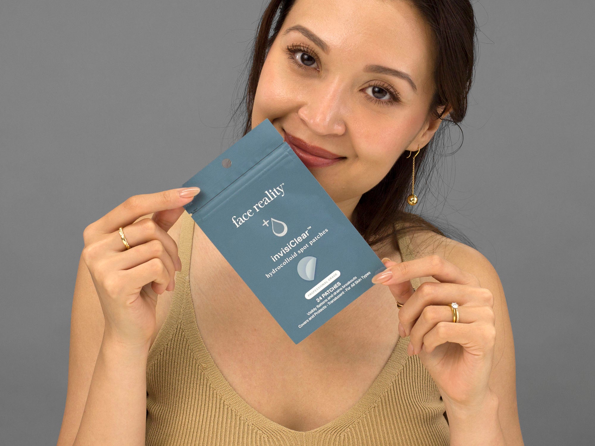 Laziza from LAZ Skincare holding a package of Face Reality InvisiClear Hydrocolloid Spot Patches up to her face