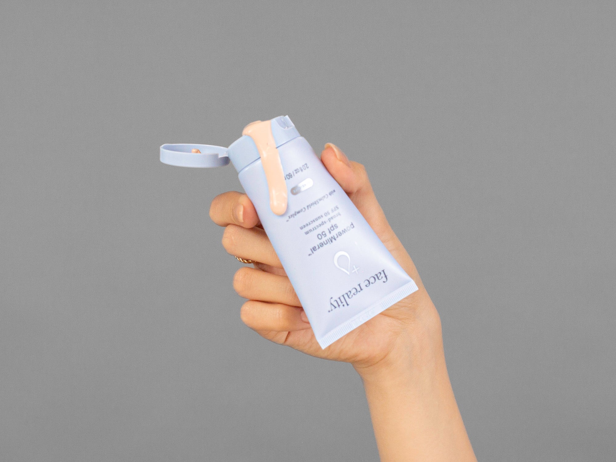 Closeup of Laziza from LAZ Skincare holding a tube of Face Reality Power Mineral SPF50 in her hand