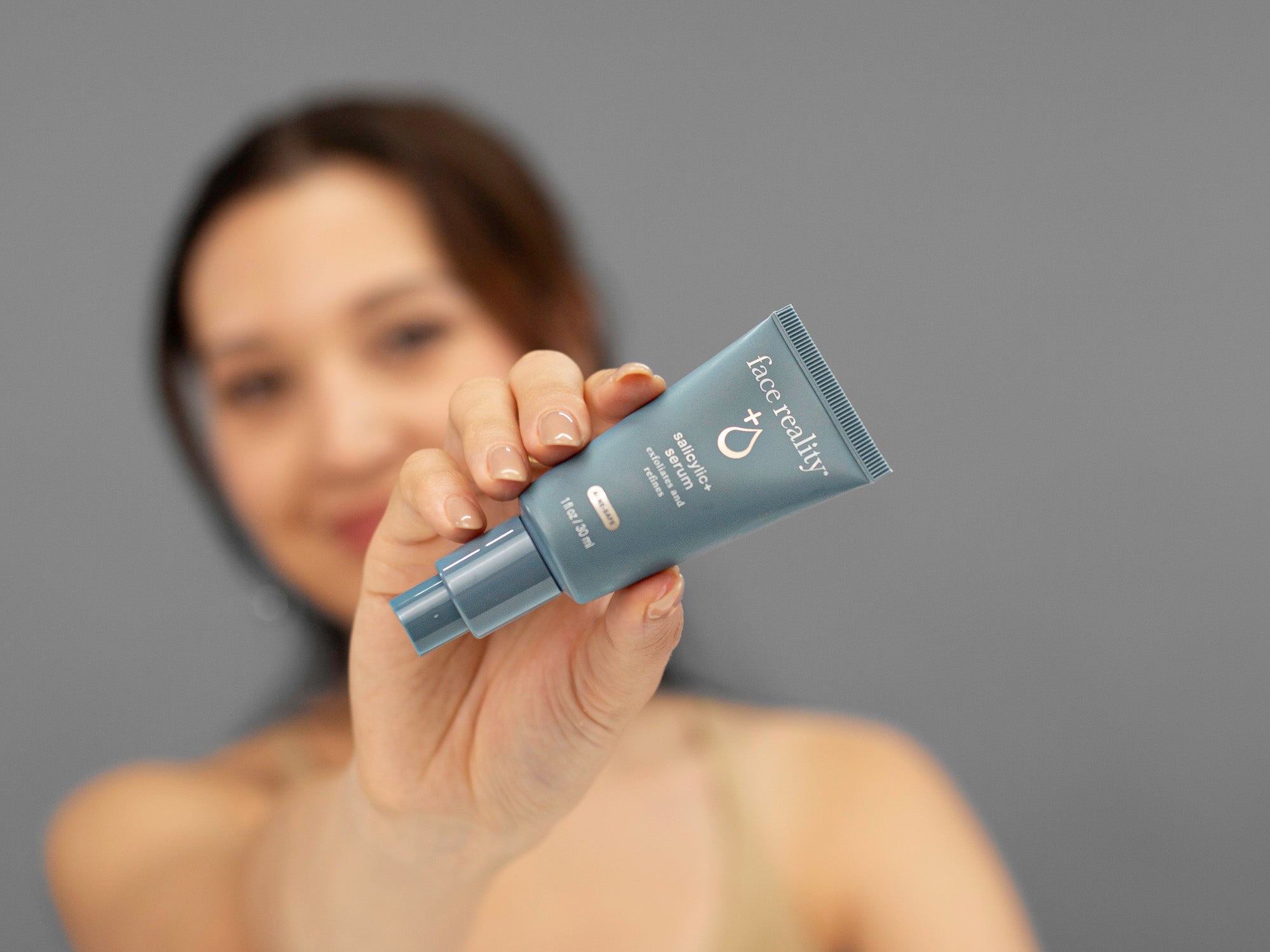 Laziza from LAZ Skincare holding up a bottle of Face Reality Salicylic Serum with a blurred background