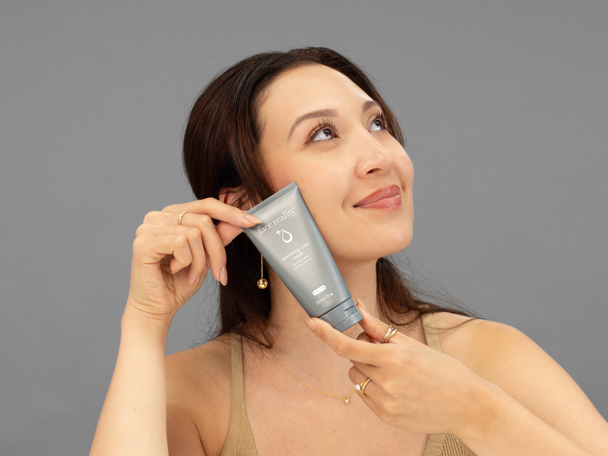 Laziza from LAZ Skincare holding a tube of Face Reality Soothing Clay Mask up to her face