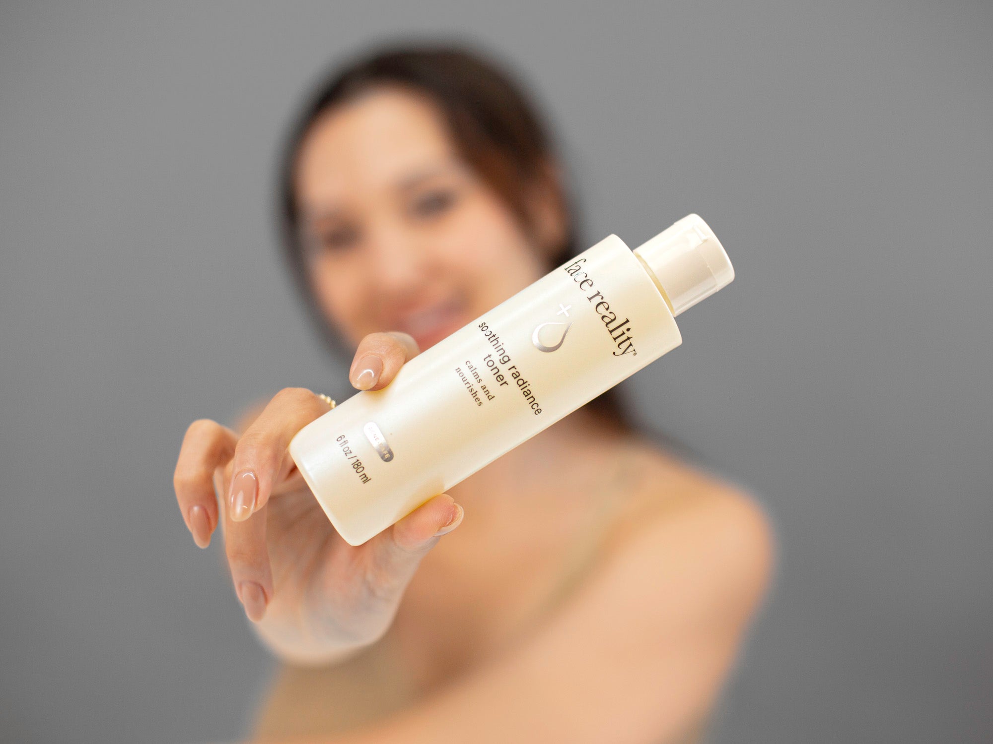 Laziza from LAZ Skincare holding a bottle of Face Reality Soothing Radiance Toner in front of her with a blurred background