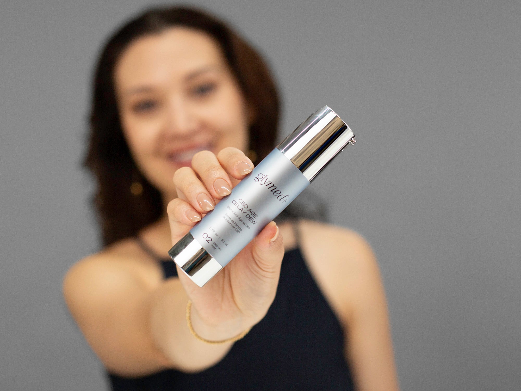 Laziza from LAZ Skincare holding up a bottle of GlyMed Hemp Age Delay Dew with a blurred background