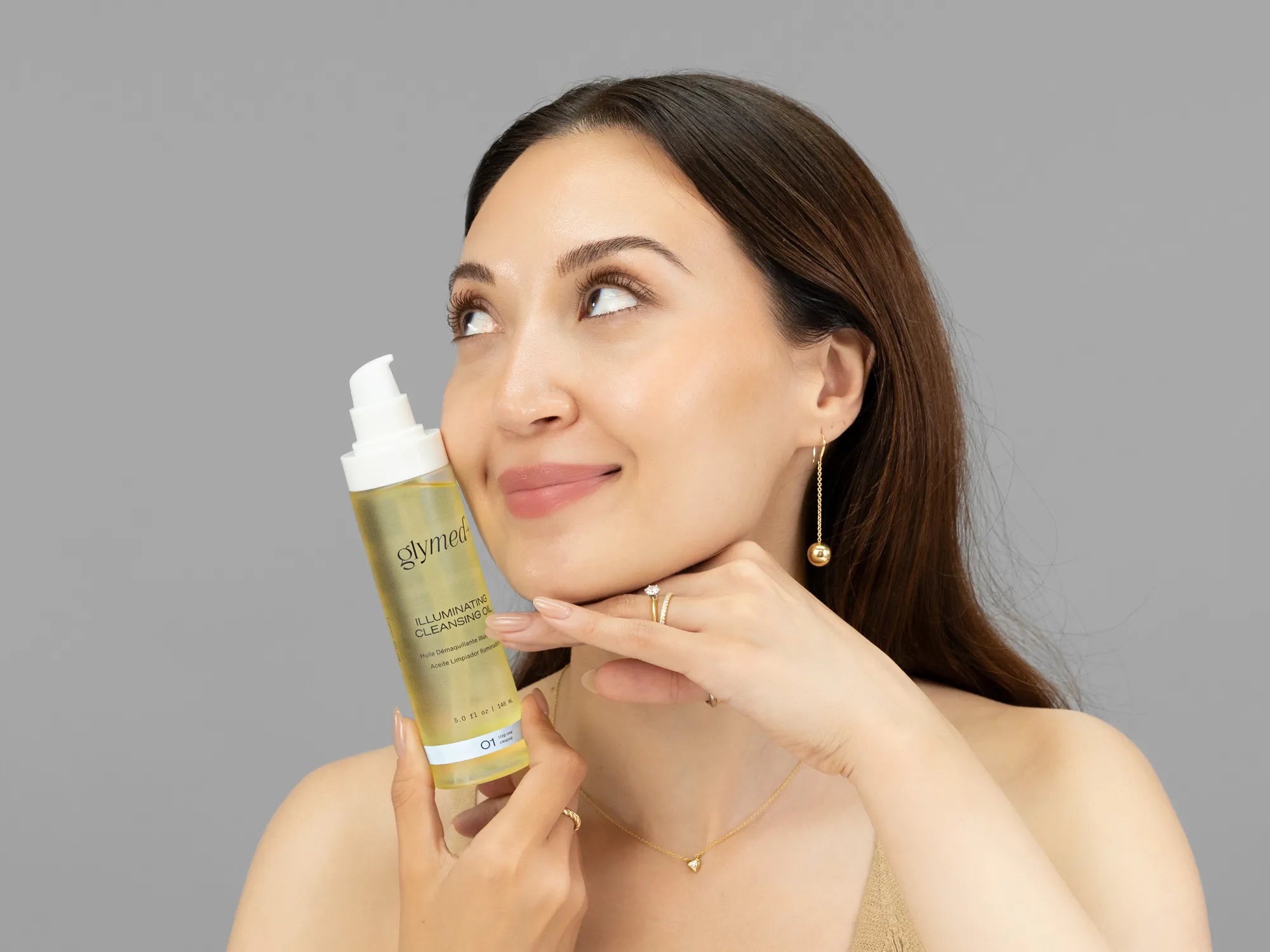 Laziza from LAZ Skincare holding a bottle of GlyMed Illuminating Cleansing Oil up to her face