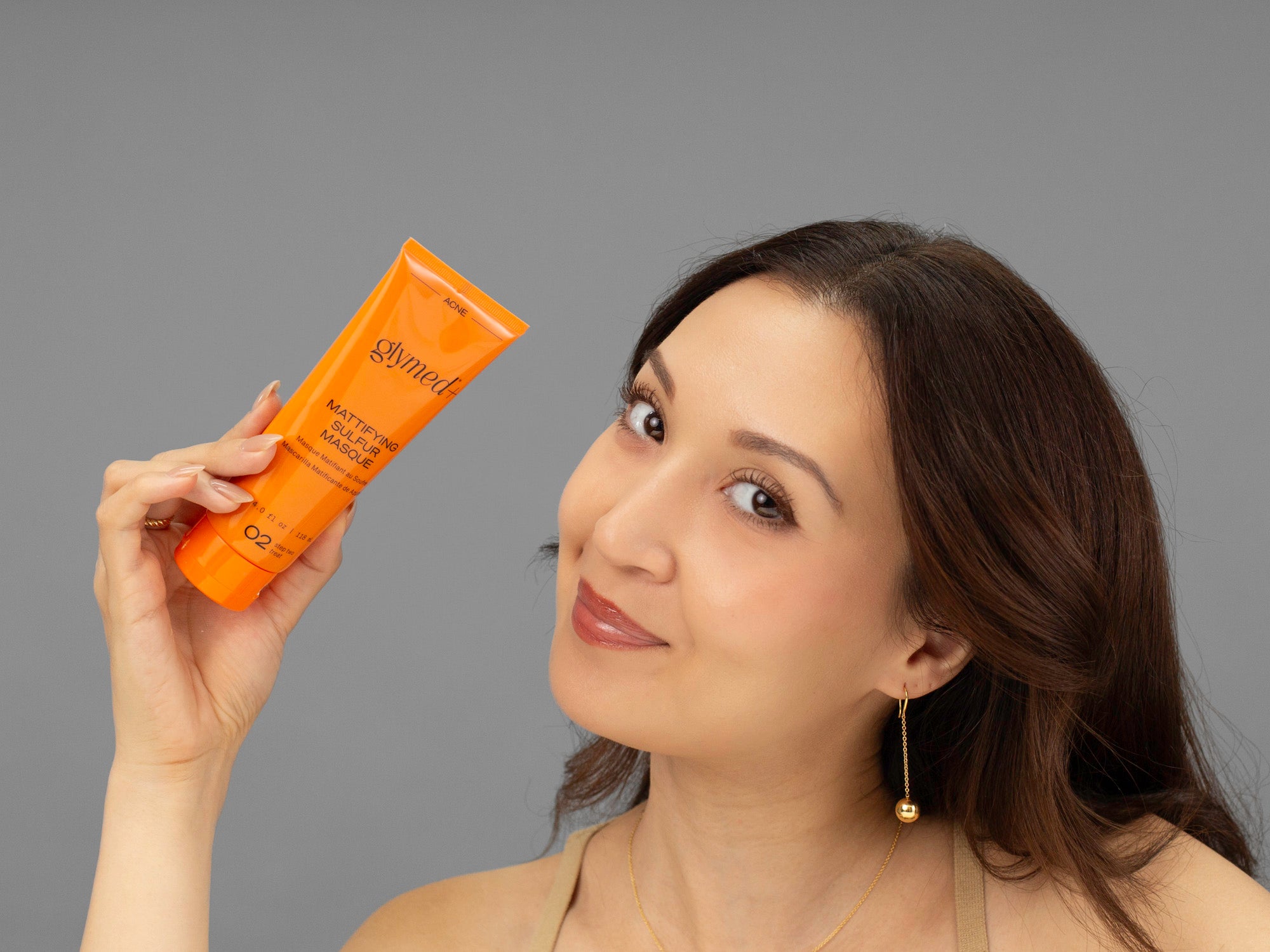 Laziza from LAZ Skincare holding a tube of GlyMed Mattifying Sulfur Masque up to her face