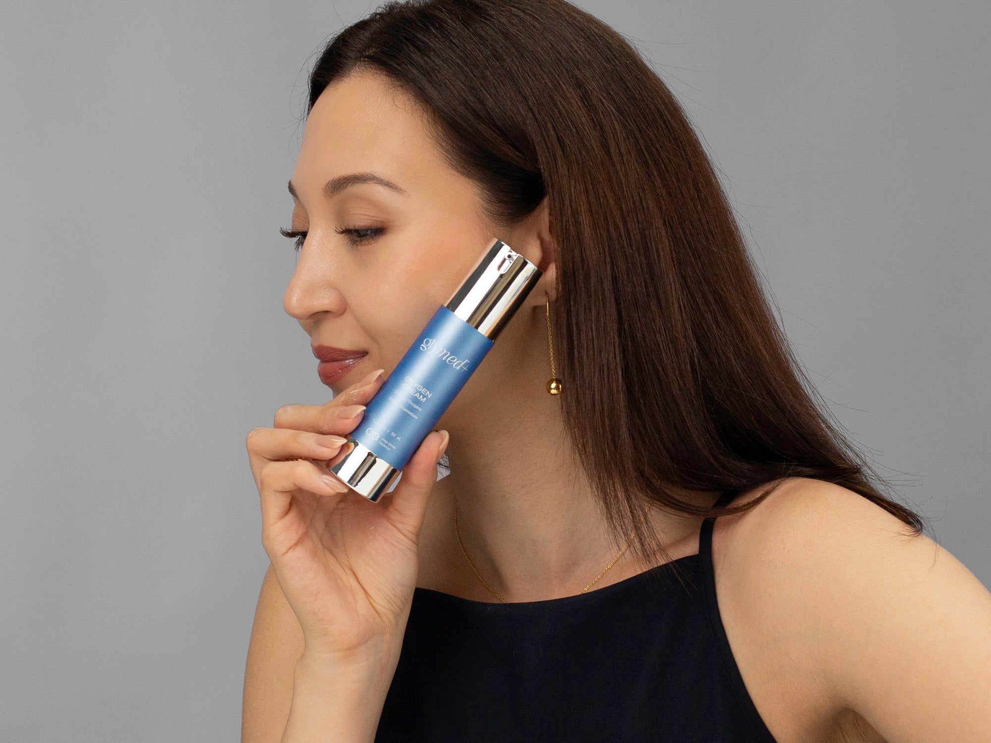 Laziza from LAZ Skincare holding a bottle of GlyMed Oxygen Cream up to her face