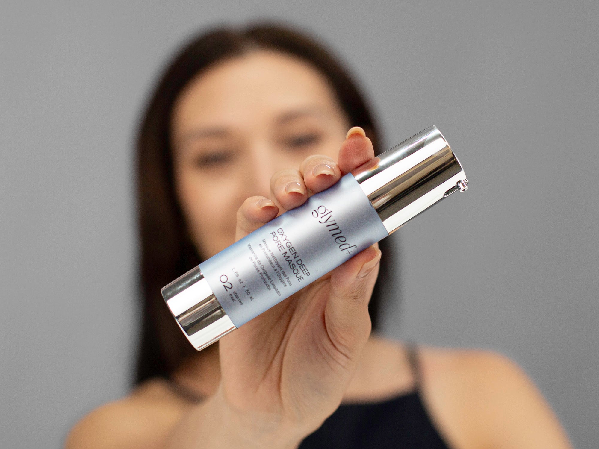 Laziza from LAZ Skincare holding up a bottle of GlyMed Oxygen Deep Pore Masque with a blurred background