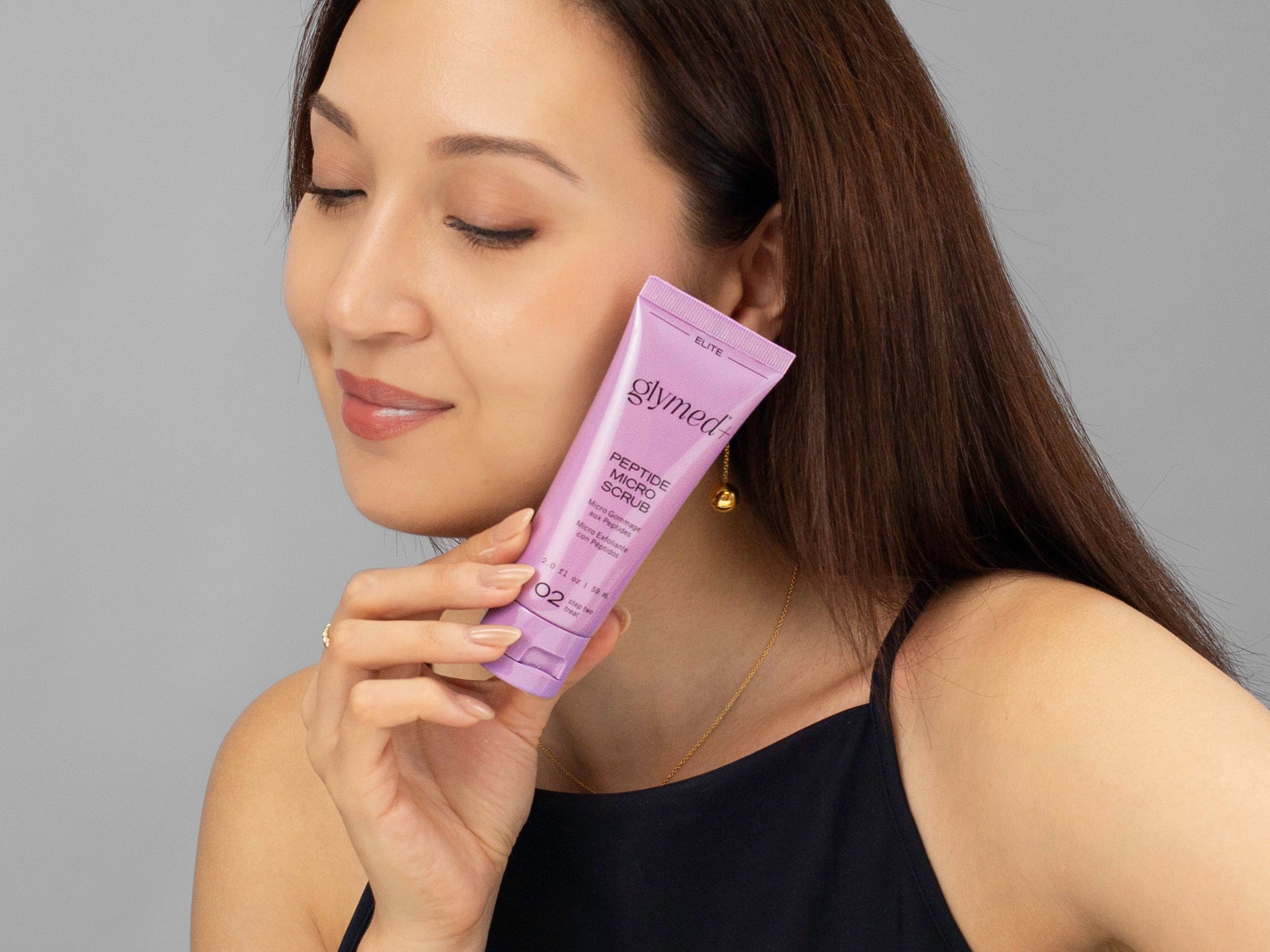 Laziza from LAZ Skincare hold a tube of GlyMed Peptide Micro Scrub up to her face