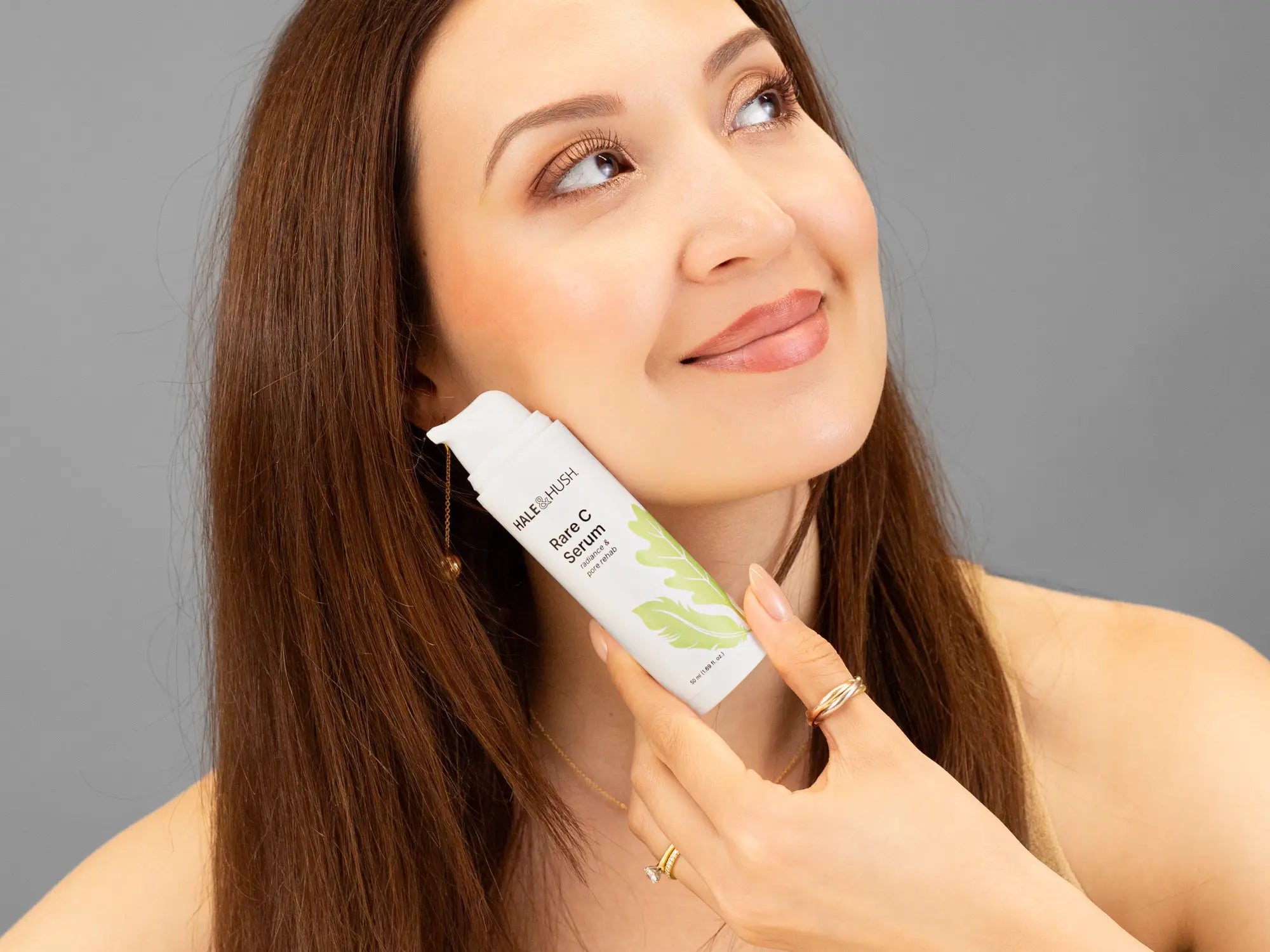Laziza from LAZ Skincare holding a bottle of Hale & Hush Rare C Serum up to her face