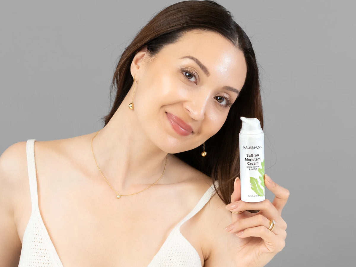 Laziza from LAZ Skincare holding a bottle of Hale & Hush Saffron Meristem Cream up to her face