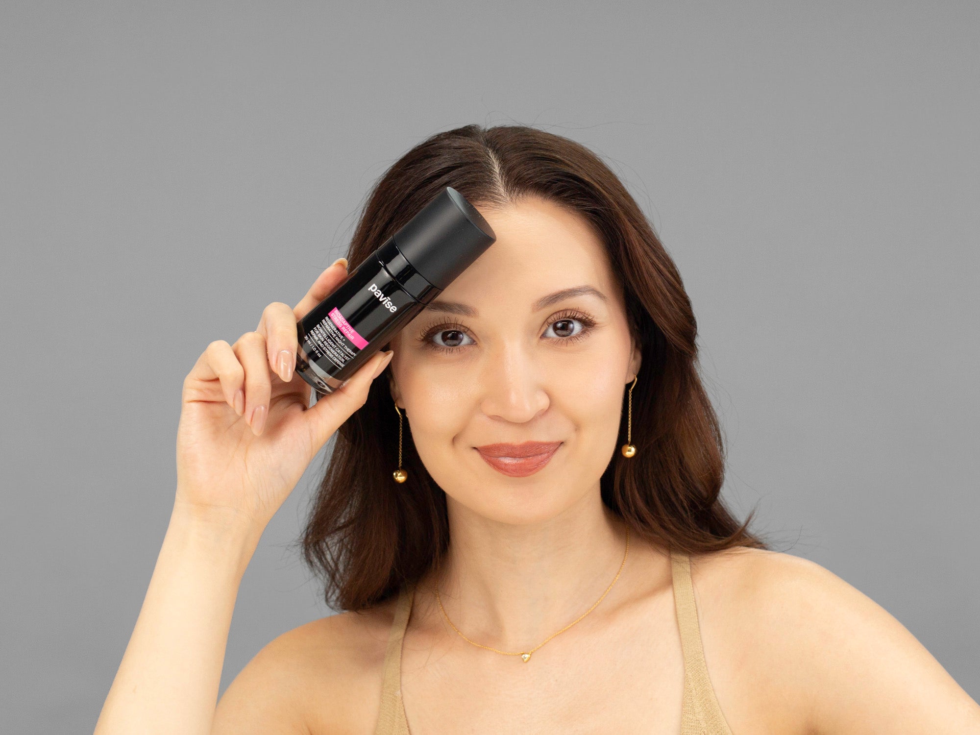 Laziza from LAZ Skincare holding a bottle of Pavise Bioadaptive Stress Repair up to her face