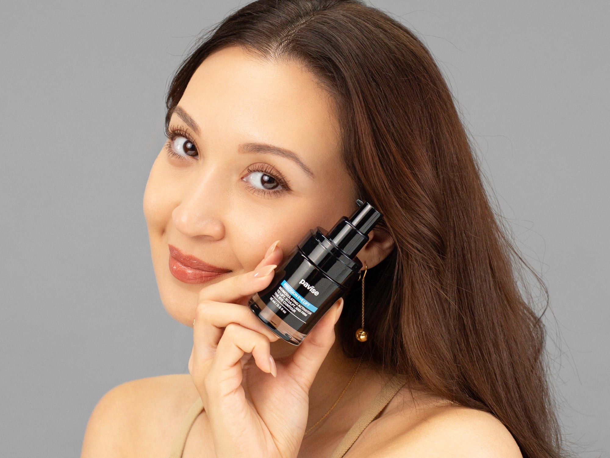 Laziza from LAZ Skincare holding a bottle of Pavise Precision Eye Lift up to her face