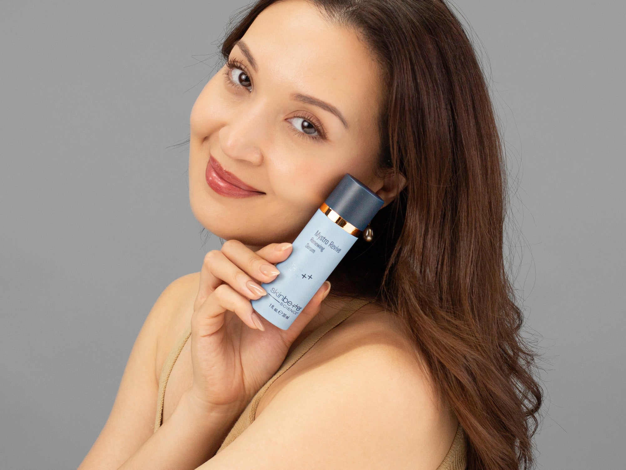 Laziza from LAZ Skincare holding a bottle of Skinbetter Science Mystro Revive Renewing Serum up to her face