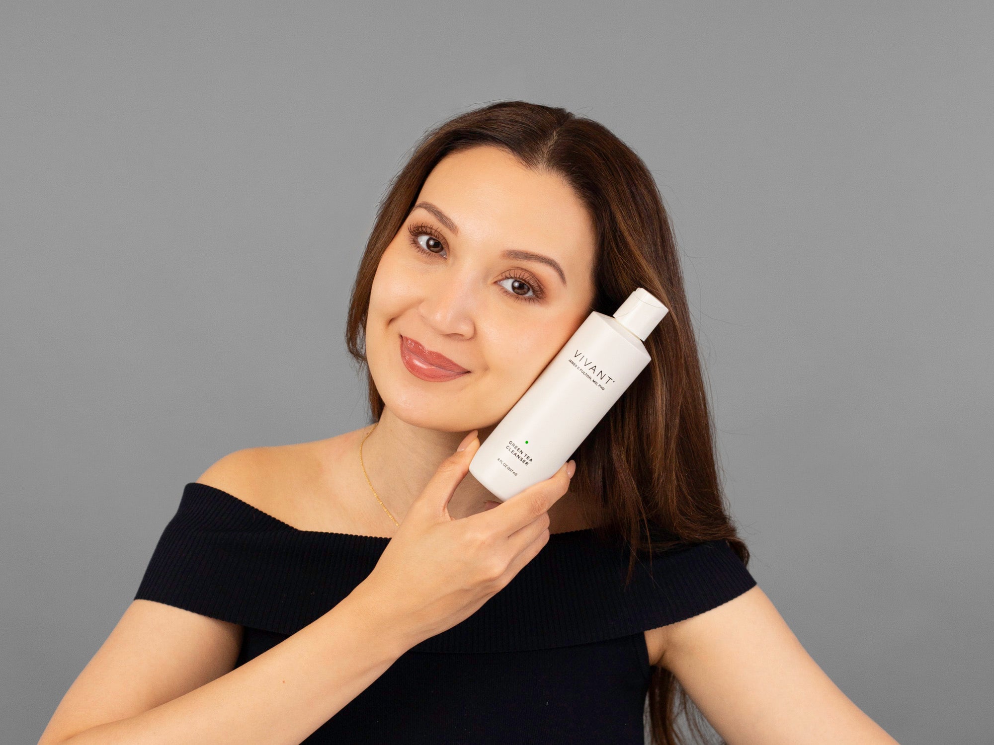 Laziza from LAZ Skincare holding a bottle of Vivant Green Tea Antioxidant Cleanser up to her face