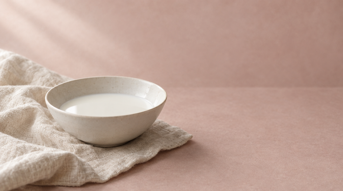 A shallow white bowl of milk on cream linen in soft daylight.