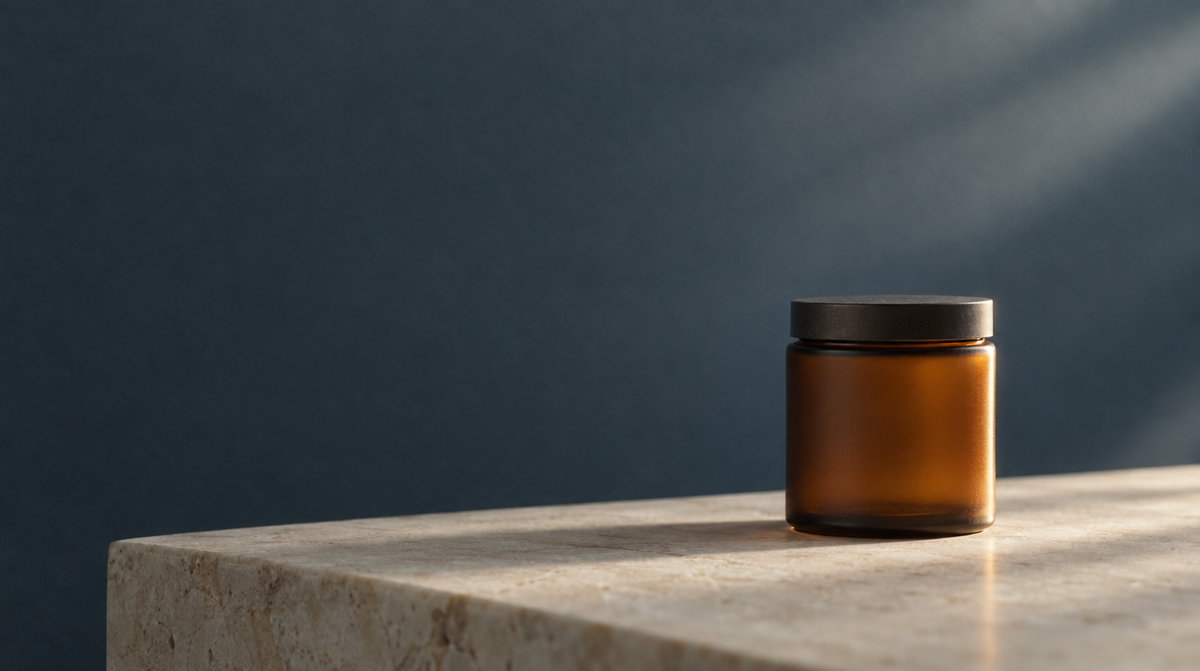 A small amber glass jar on a pale stone surface in soft directional light.