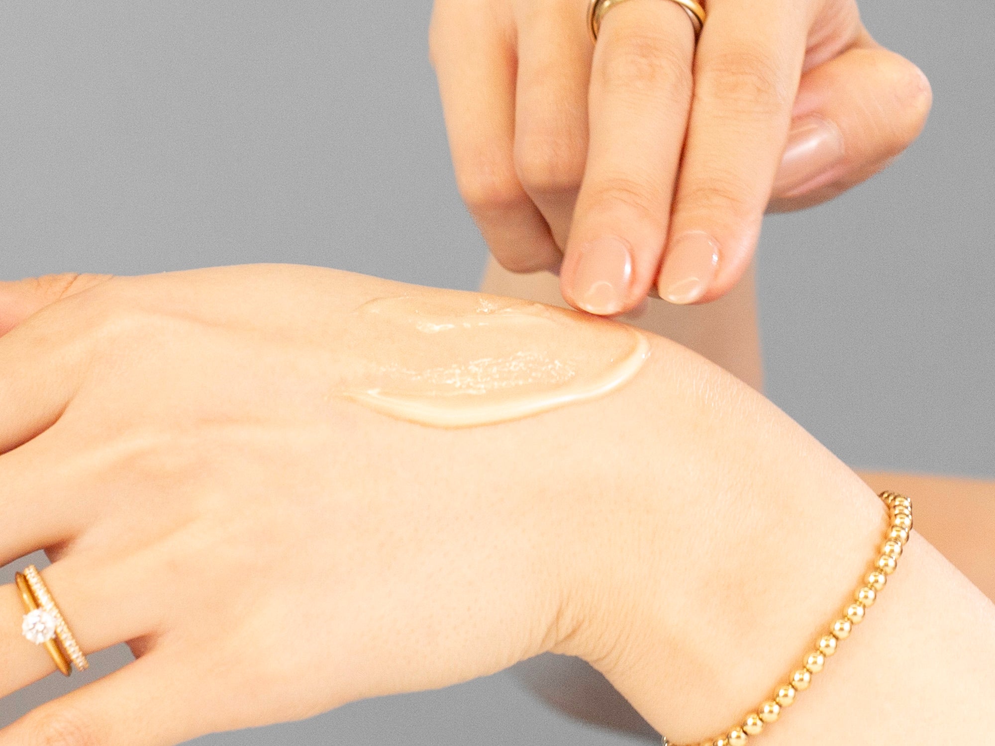 Laziza from LAZ Skincare applying Alastin C-Radical Defense Antioxidant Serum cream to her hand with a gray background