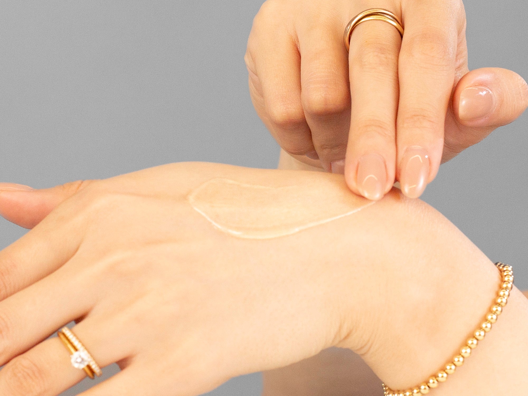 Laziza from LAZ Skincare applying Alastin Regenerating Skin Nectar to her hand on a neutral background