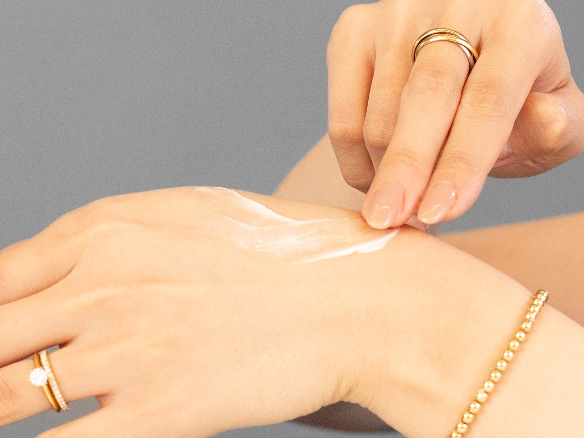 Laziza from LAZ Skincare applying Alastin Restorative Neck Complex cream to another hand with a neutral background