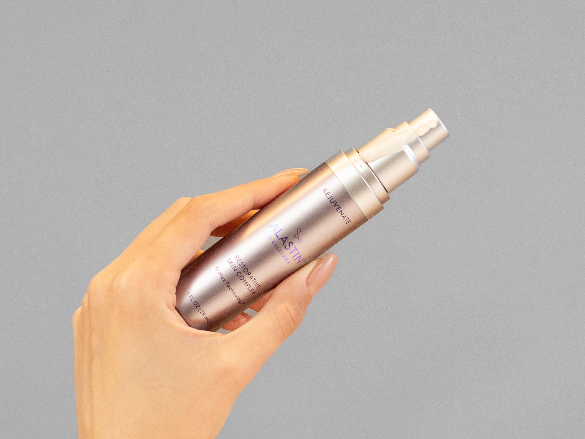 Laziza from LAZ Skincare holding a silver Alastin Restorative Skin Complex bottle against a gray background