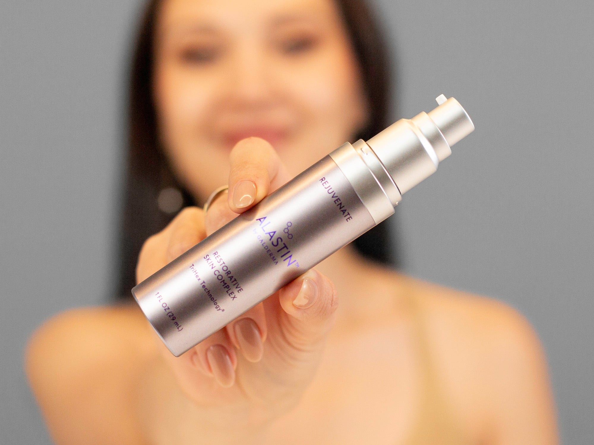 Laziza from LAZ Skincare holding a silver Alastin Restorative Skin Complex bottle with a blurred background