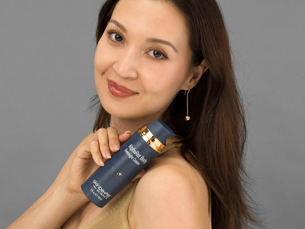 Laziza from LAZ Skincare holding a bottle of SkinBetter Science AlphaRet Body Overnight Cream up to her face