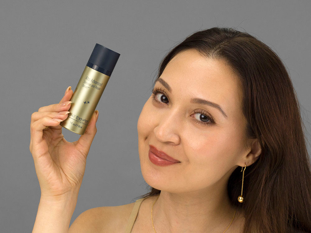 Laziza from LAZ Skincare holding a bottle of SkinBetter Science Alto Advanced Defense and Repair Serum up to her face