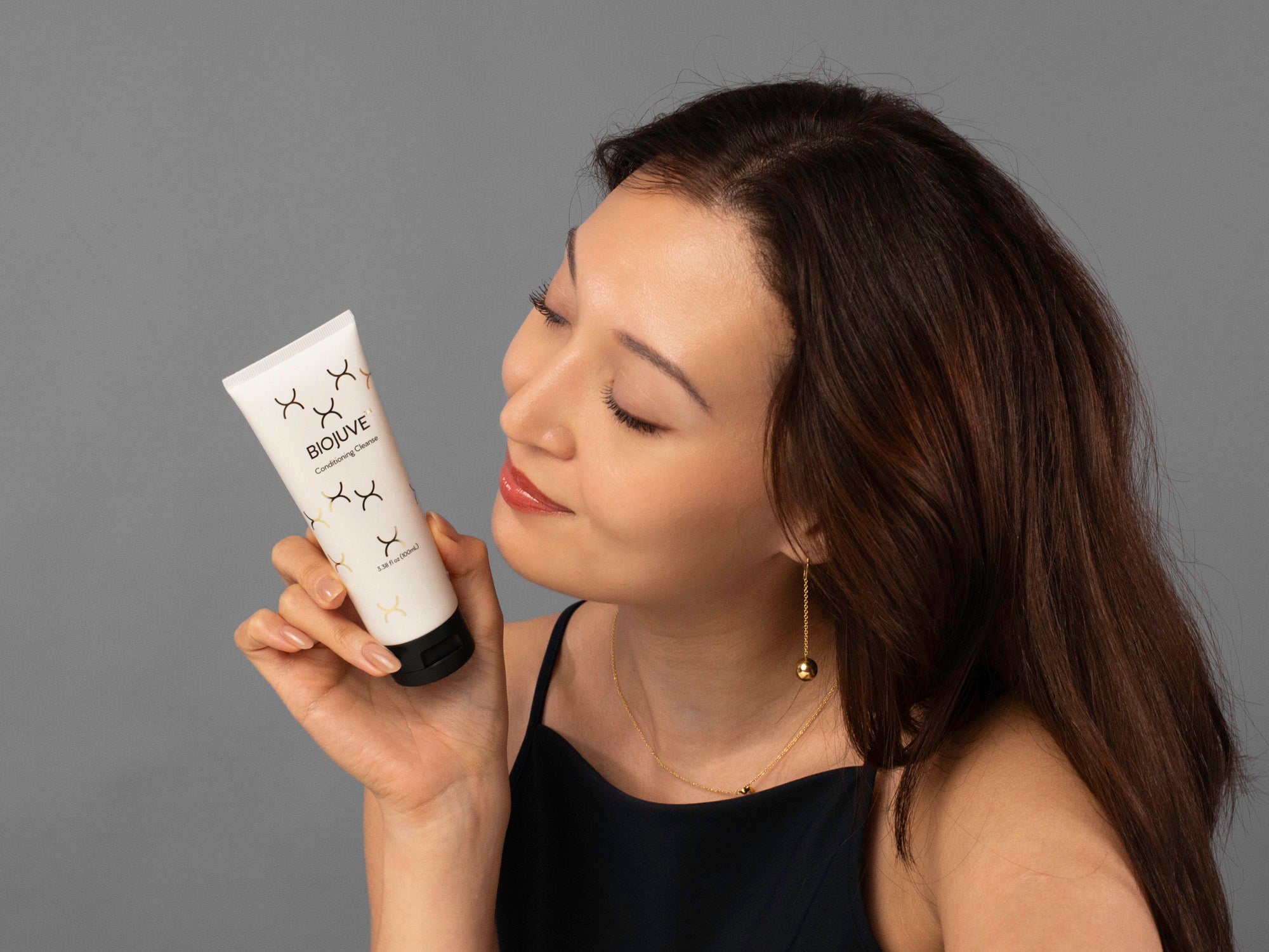 Laziza from LAZ Skincare holding a tube of BioJuve Conditioning Cleanse up to her face