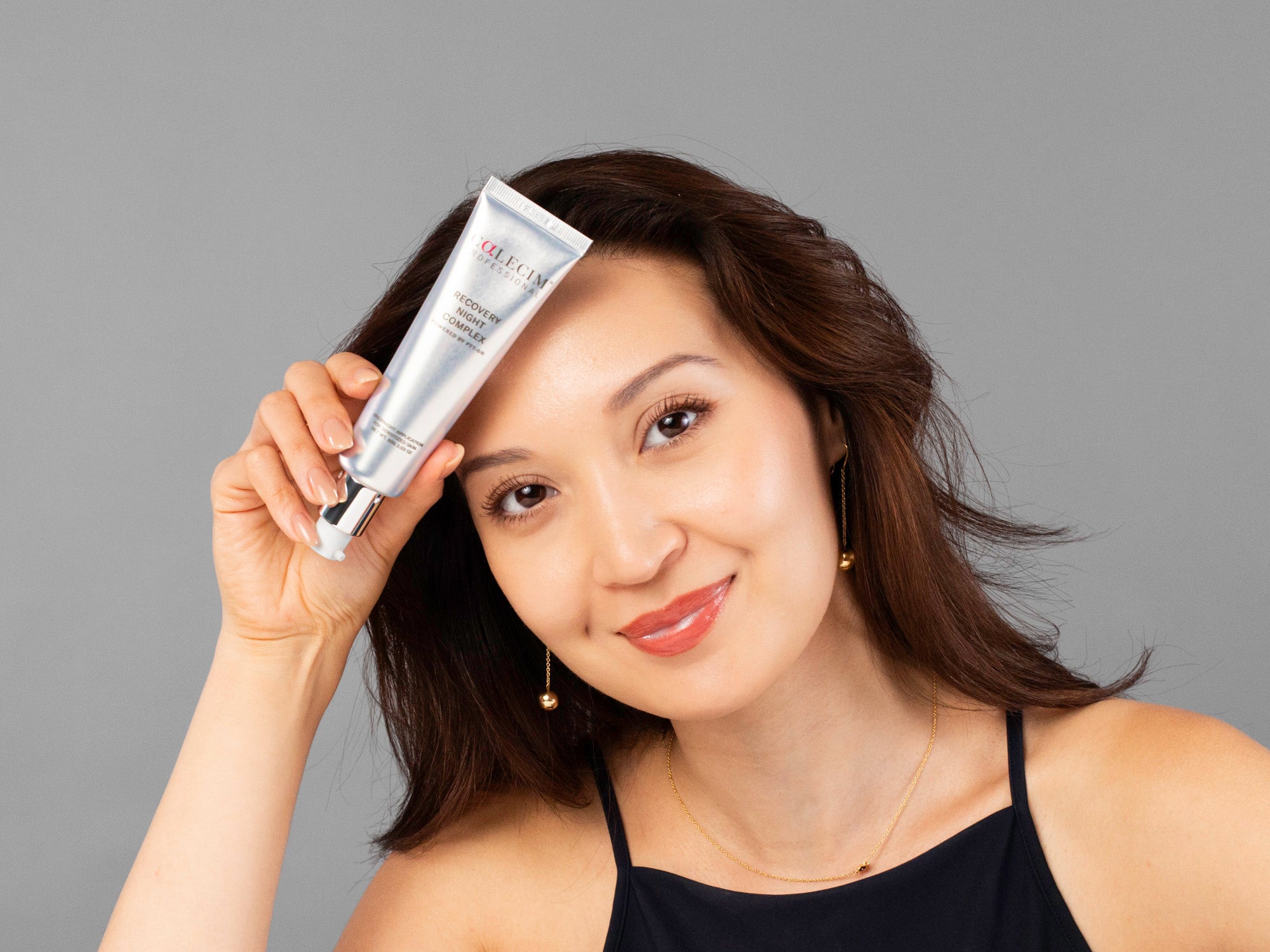 Laziza from LAZ Skincare holding a tube of Calecim Recovery Night Complex up to her face