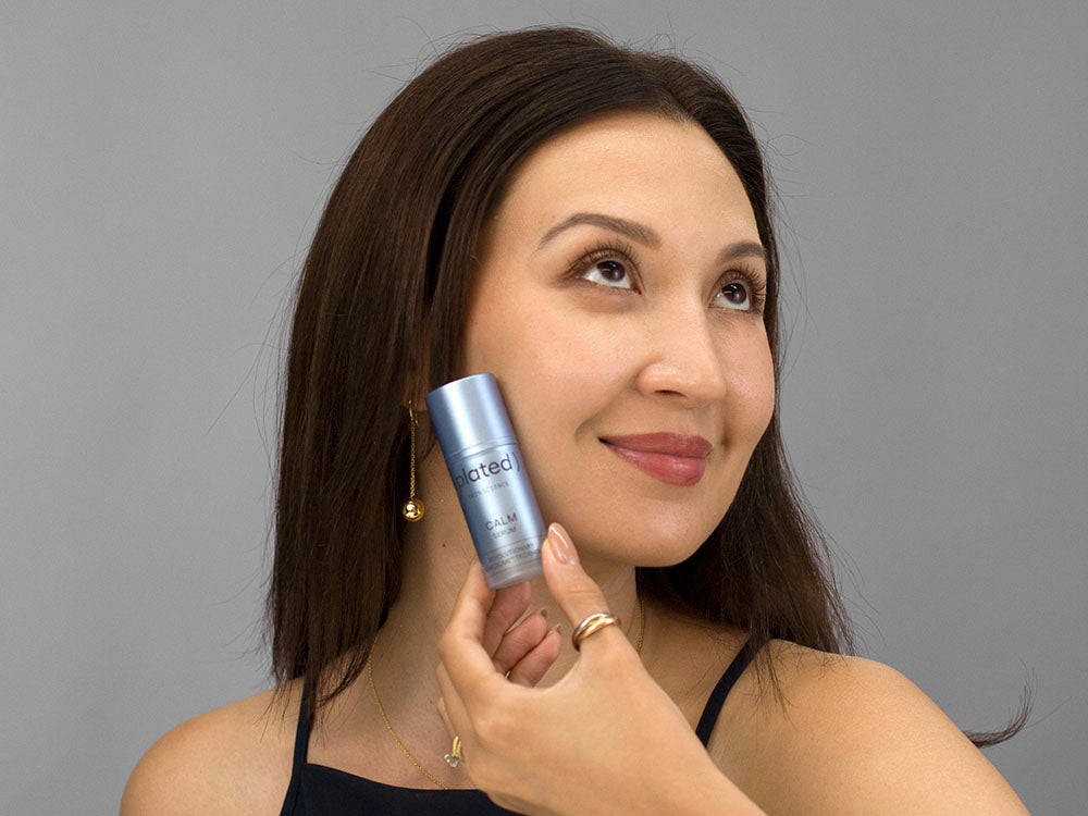 Laziza from LAZ Skincare holding a bottle of Plated Calm Serum up to her face