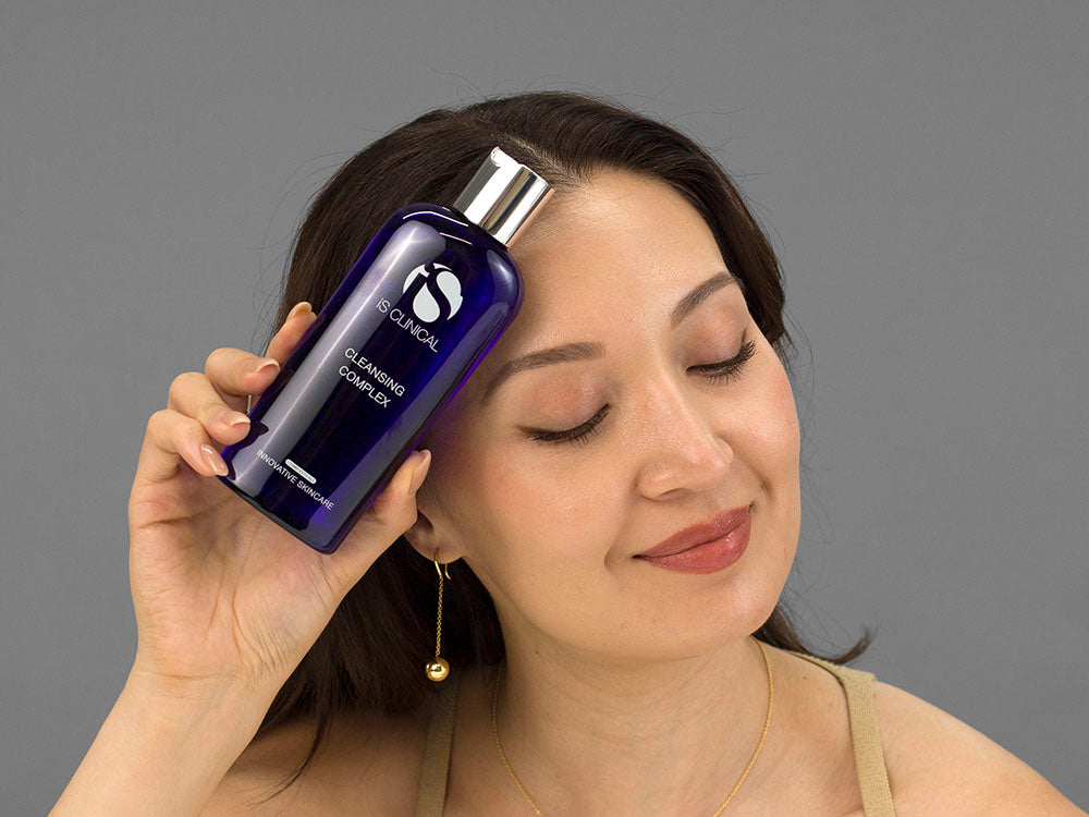 Laziza from LAZ Skincare holding a bottle of iS Clinical Cleansing Complex up to her face