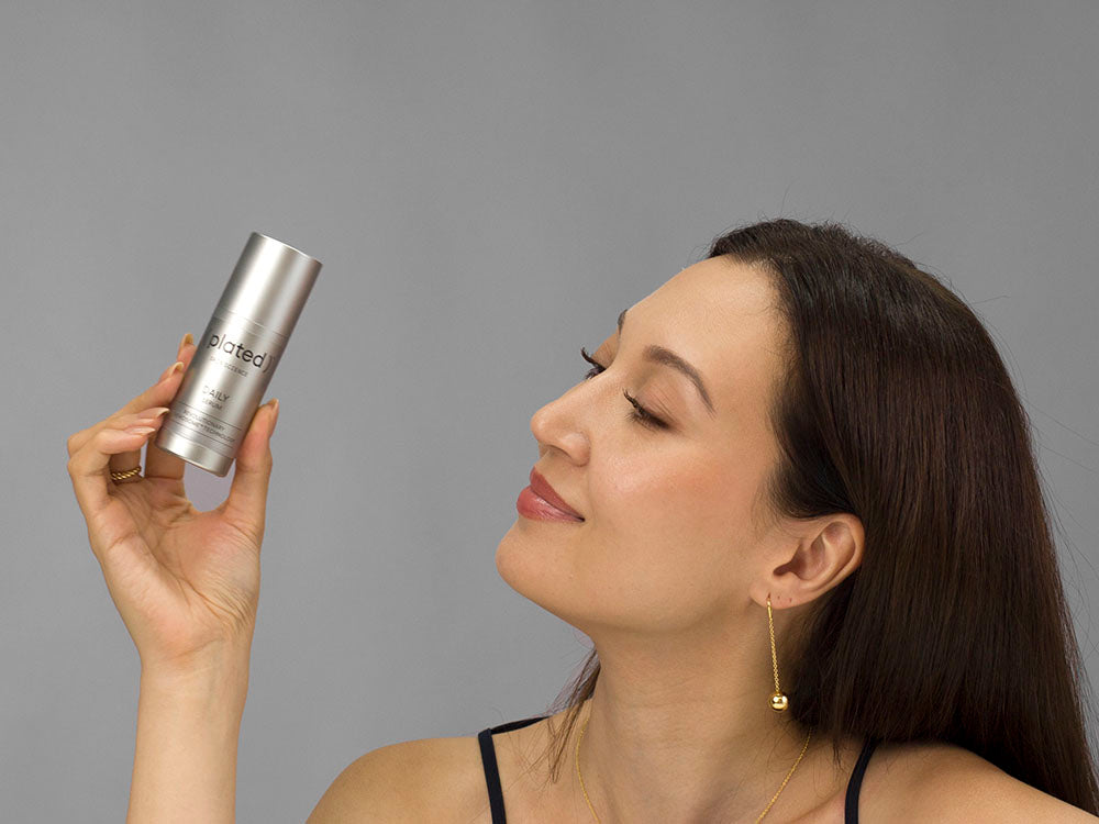 Laziza from LAZ Skincare holding a bottle of Plated Daily Serum up to her face