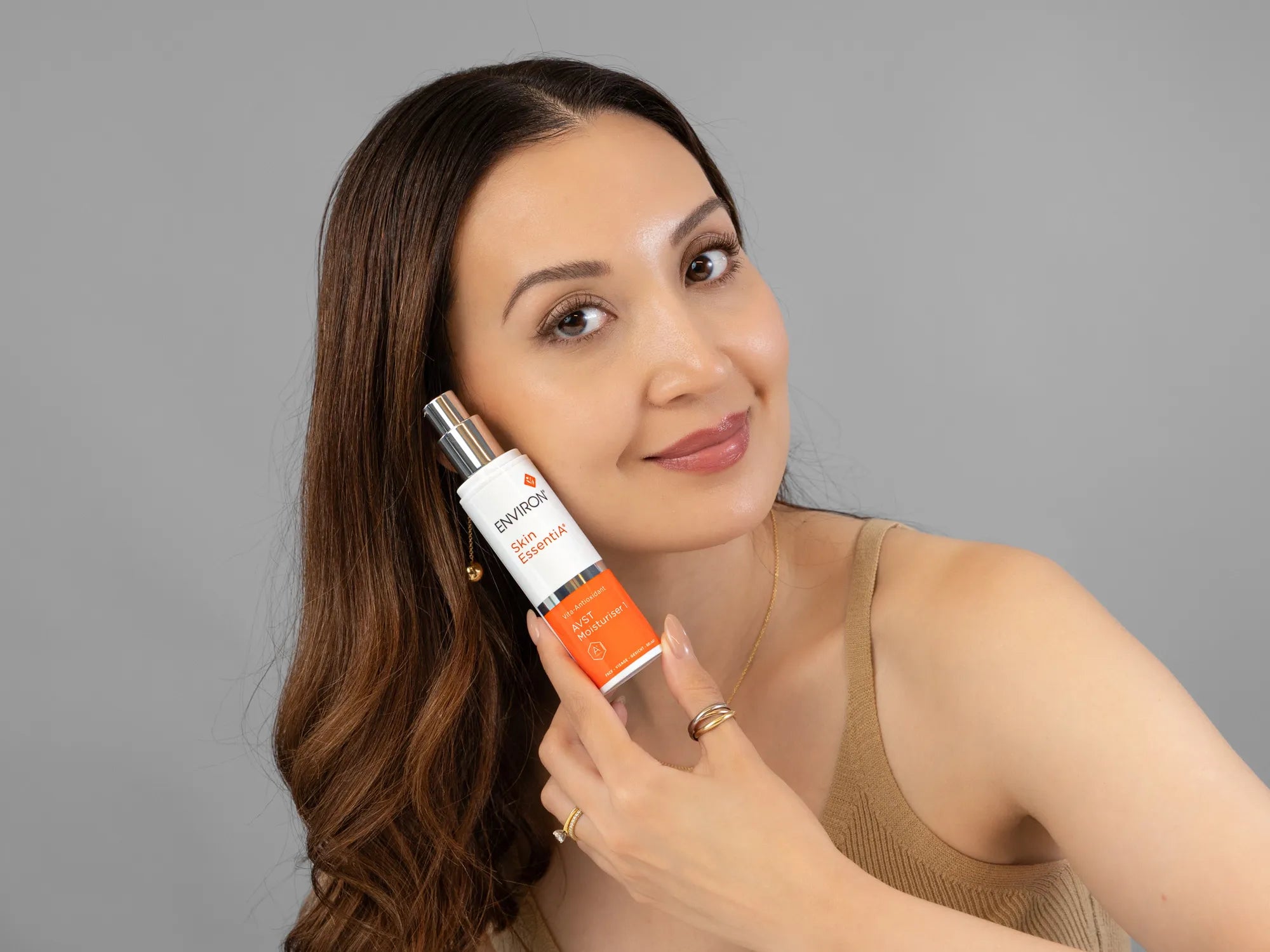 Laziza from LAZ Skincare holding a bottle of Environ AVST Moisturiser up to her face