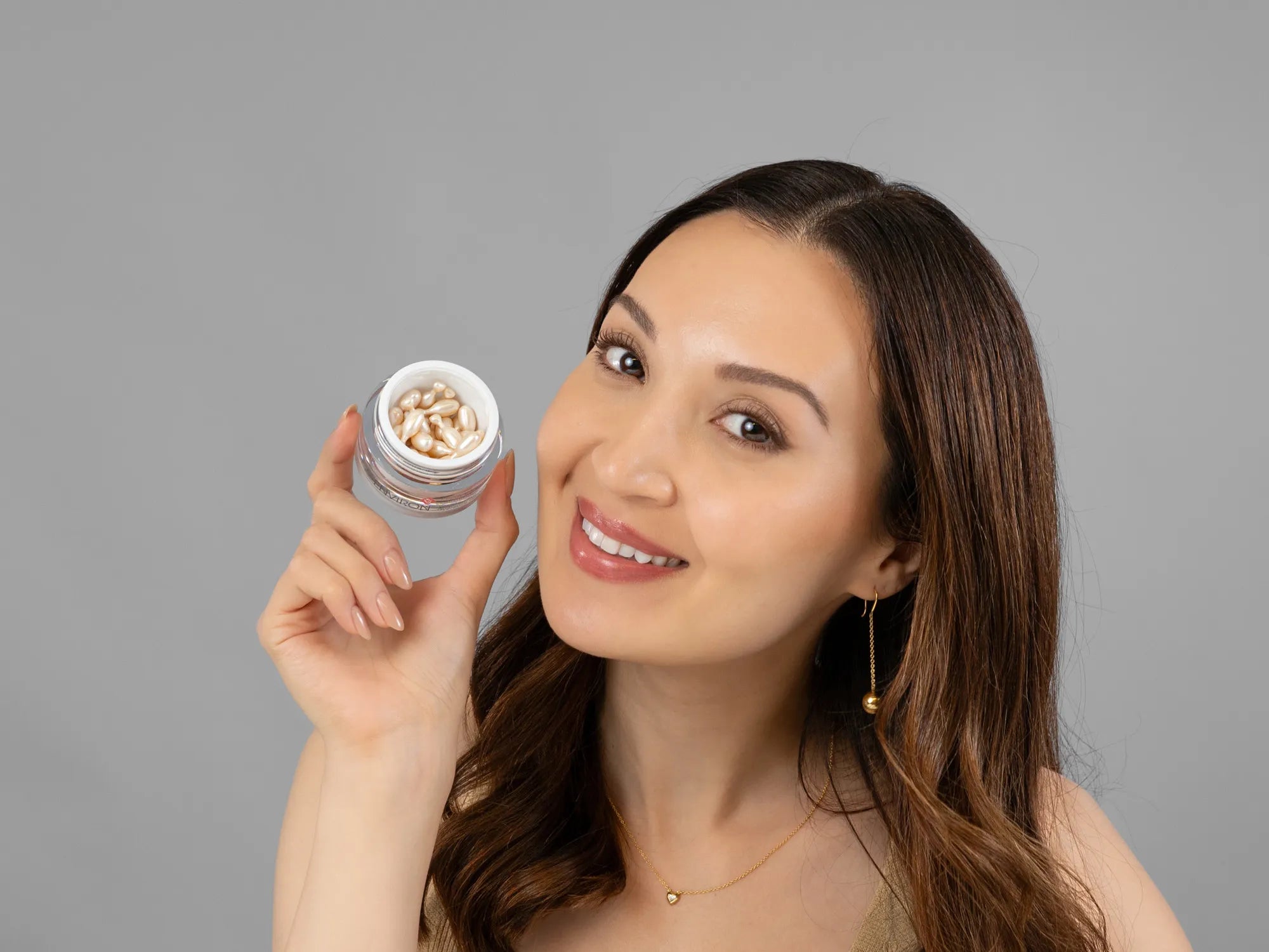 Laziza from LAZ Skincare holding a bottle of Environ Hydrating Oil Capsules up to her face