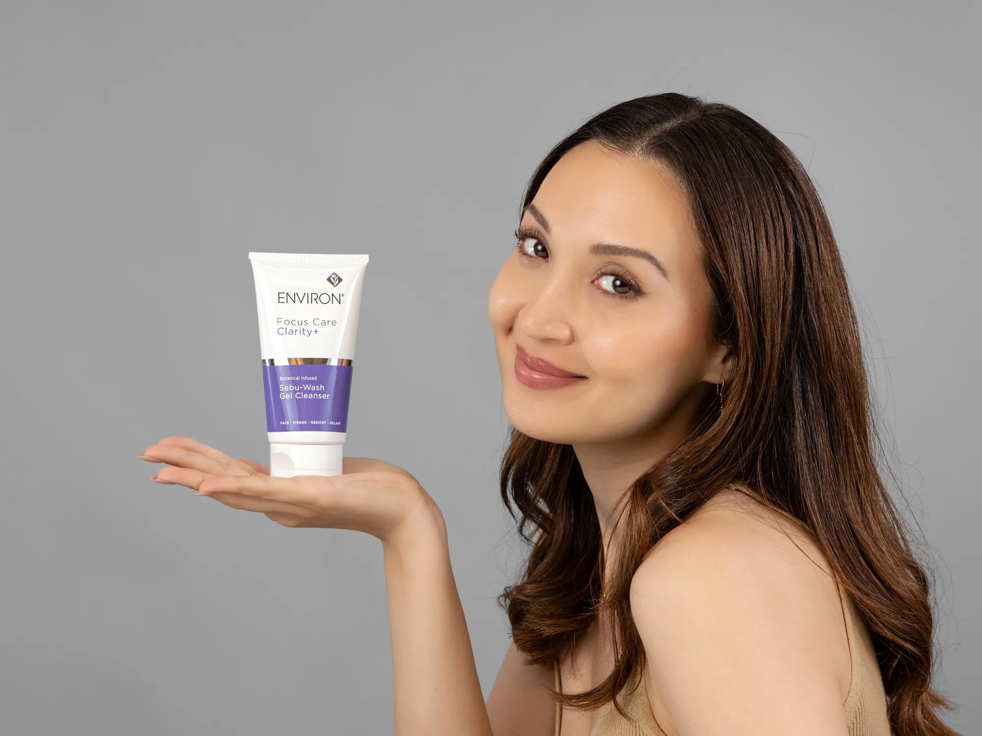 Laziza from LAZ Skincare holding a bottle of Environ Sebu-Wash Gel Cleanser up to her face
