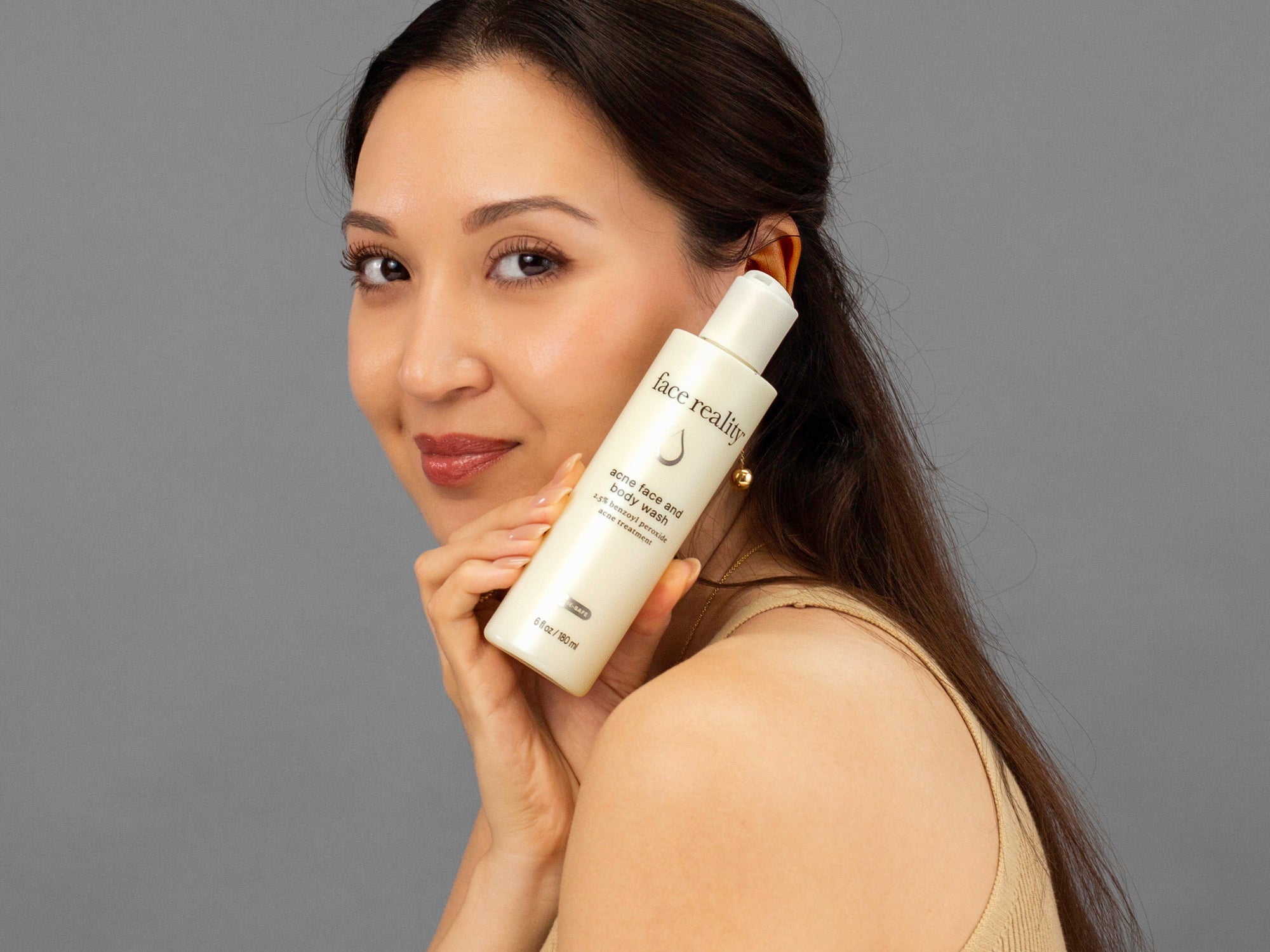 Laziza from LAZ Skincare holding a bottle of Face Reality Acne Face & Body Wash up to her face