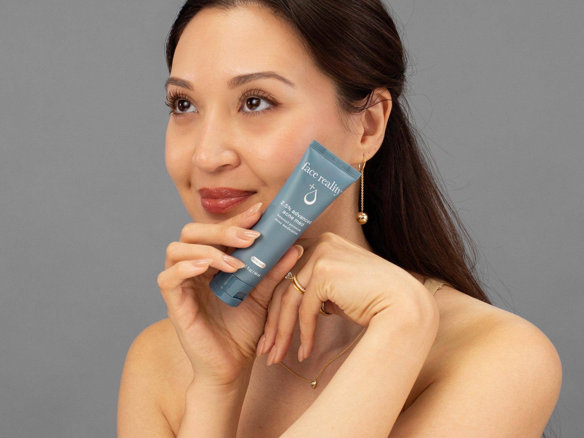 Laziza from LAZ Skincare holding a tube of Face Reality Advanced Acne Med up to her face