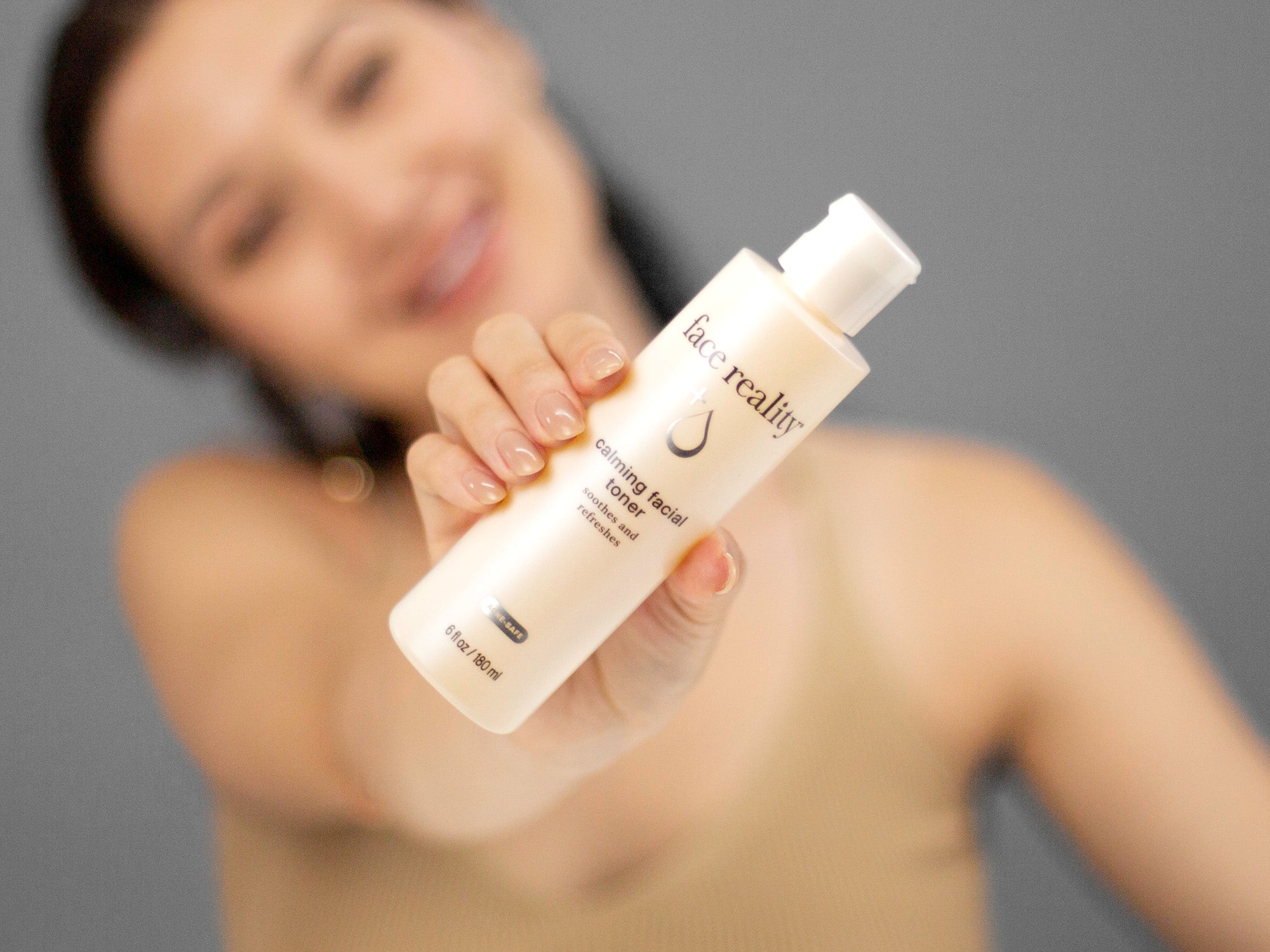 Laziza from LAZ Skincare holding up a bottle of Face Reality Calming Facial Toner with a blurred background