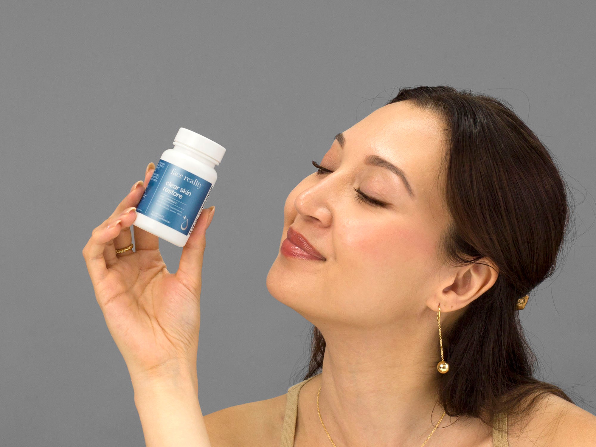 Laziza from LAZ Skincare holding a bottle of Face Reality Clear Skin Restore supplements up to her face