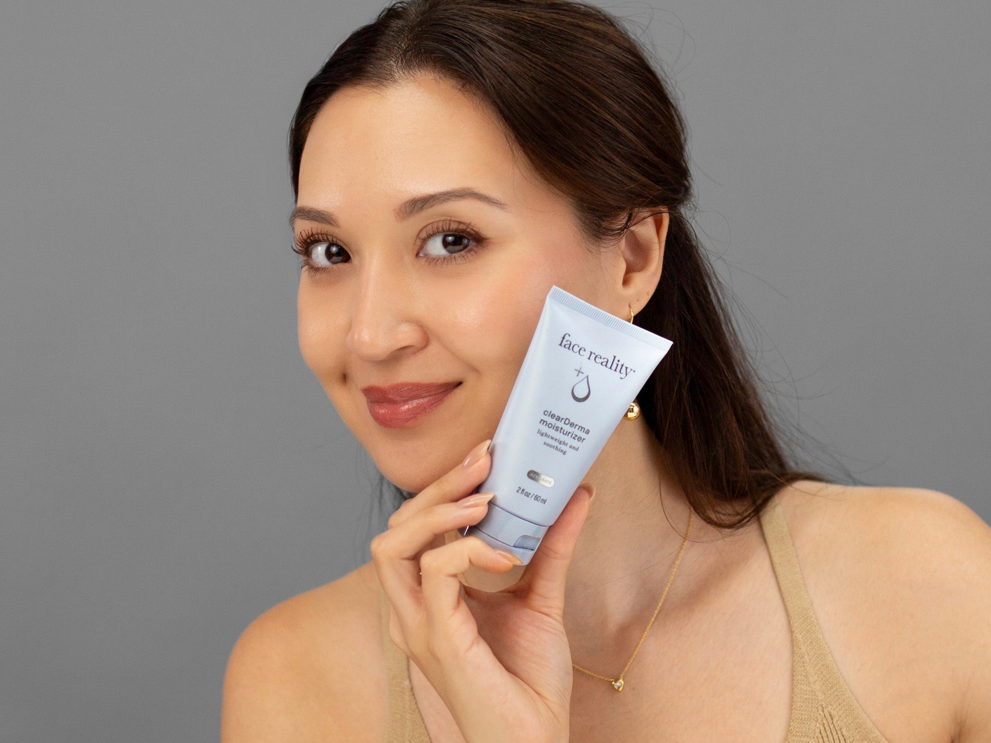 Laziza from LAZ Skincare holding a tube of Face Reality Clearderma Moisturizer up to her face