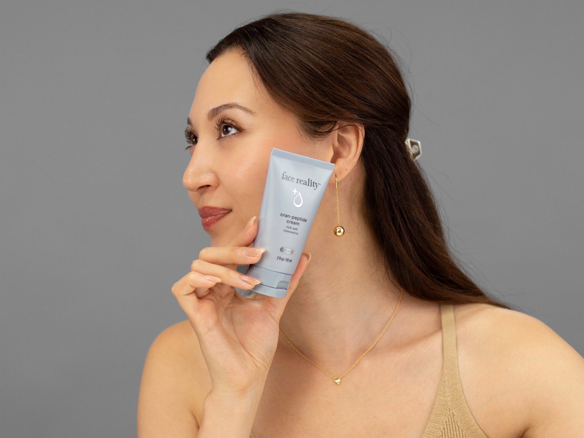 Laziza from LAZ Skincare holding a tube of Face Reality Cran-Peptide Cream up to her face