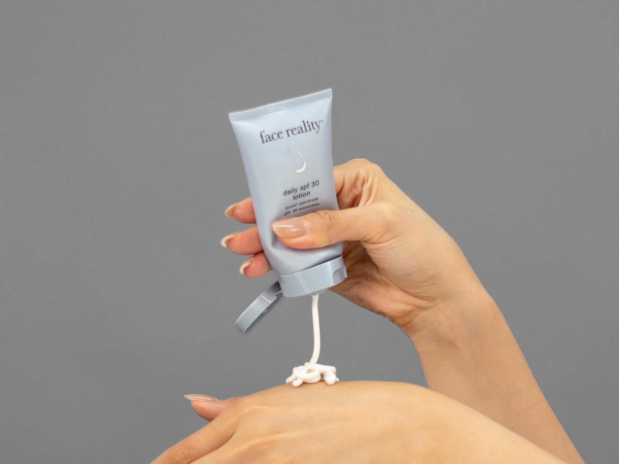 Closeup of Laziza from LAZ Skincare squeezing a tube of Face Reality Daily SPF30 Plus sunscreen onto her hand